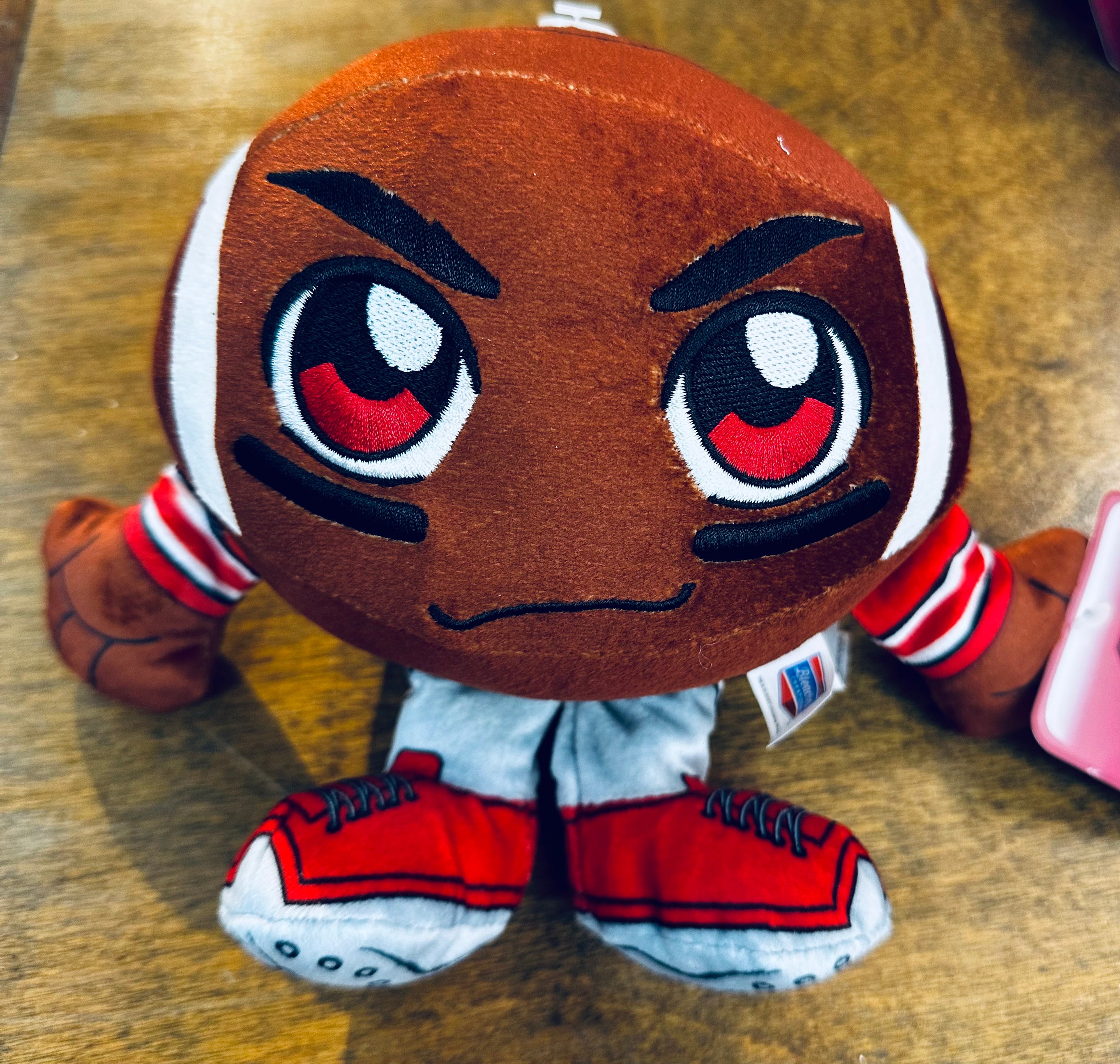 Plush toy resembling a character with large eyes and red shoes on a wooden surface