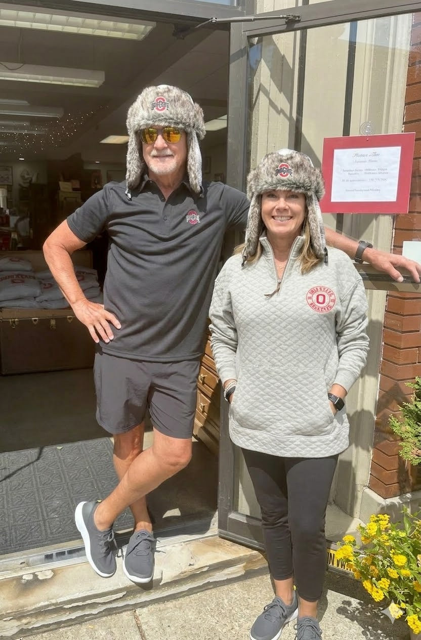 Two people wearing matching gray fur hats standing outside a building.