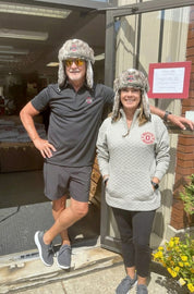 Two people wearing matching gray fur hats standing outside a building.