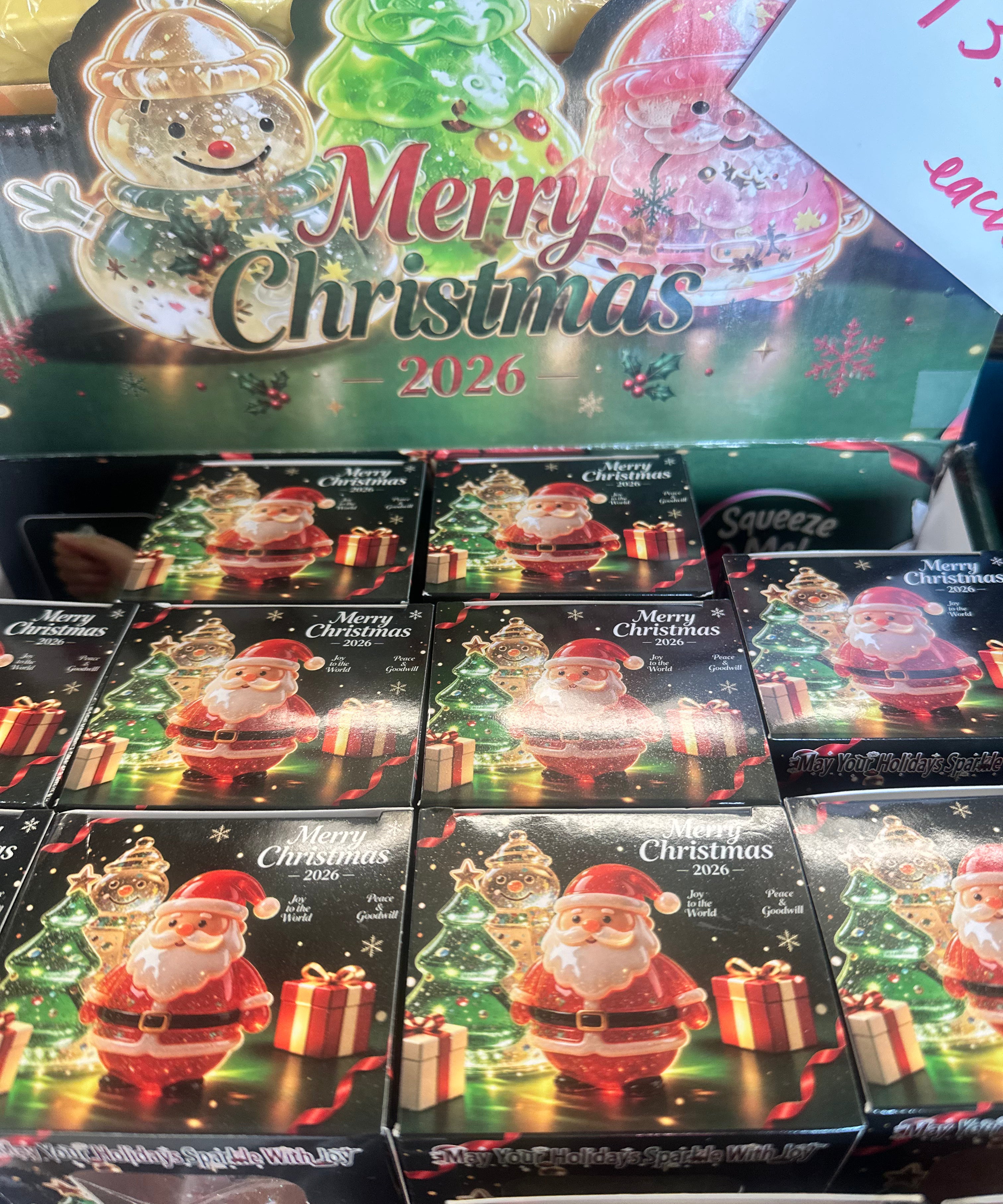A retail display of Santa Claus Christmas ornament boxes with 'Merry Christmas 2026' holiday graphics on the packaging, photographed in a store setting.