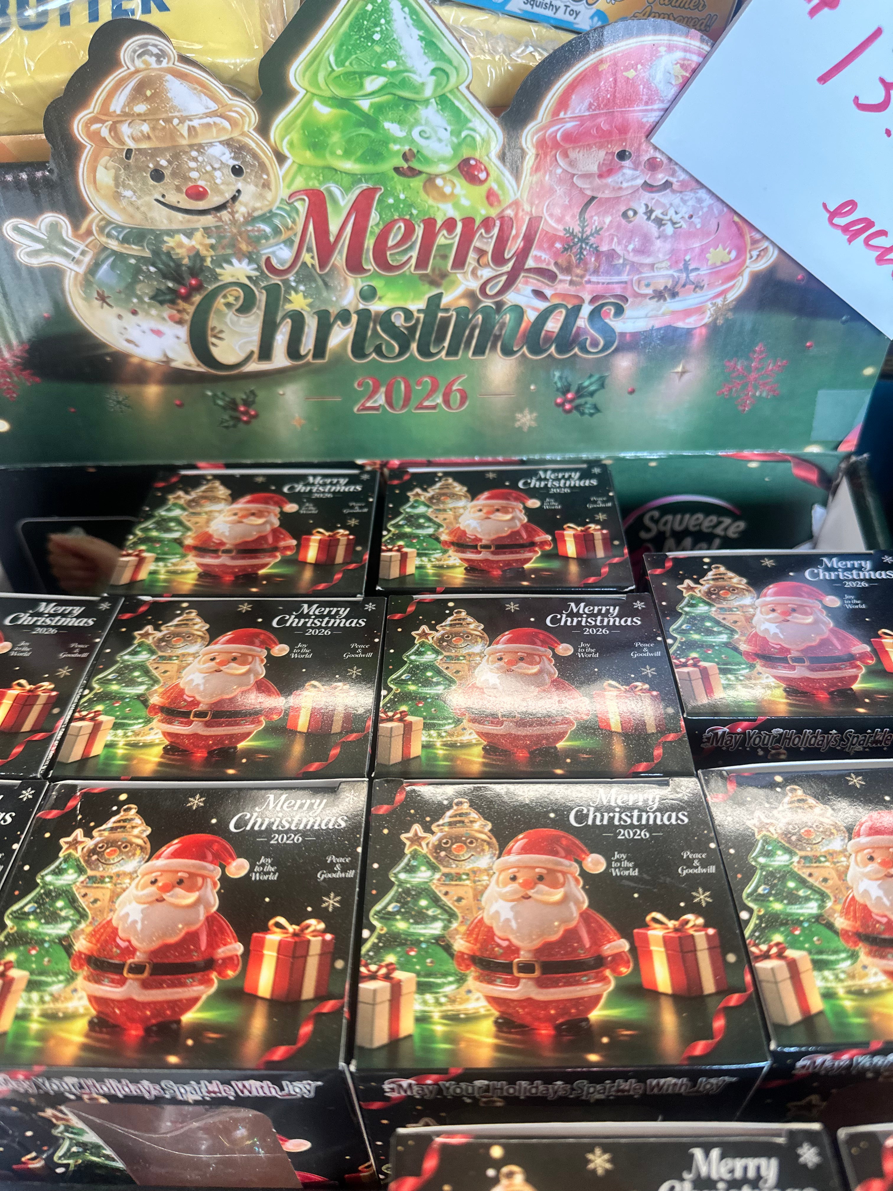 A retail display of Santa Claus Christmas ornament boxes with 'Merry Christmas 2026' holiday graphics on the packaging, photographed in a store setting.