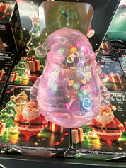 A pink glittery Christmas ornament-shaped container with a clear Santa hat and colorful heart-shaped embellishments, displayed in front of holiday-themed packaging featuring Santa Claus and 'Merry Christmas' designs.