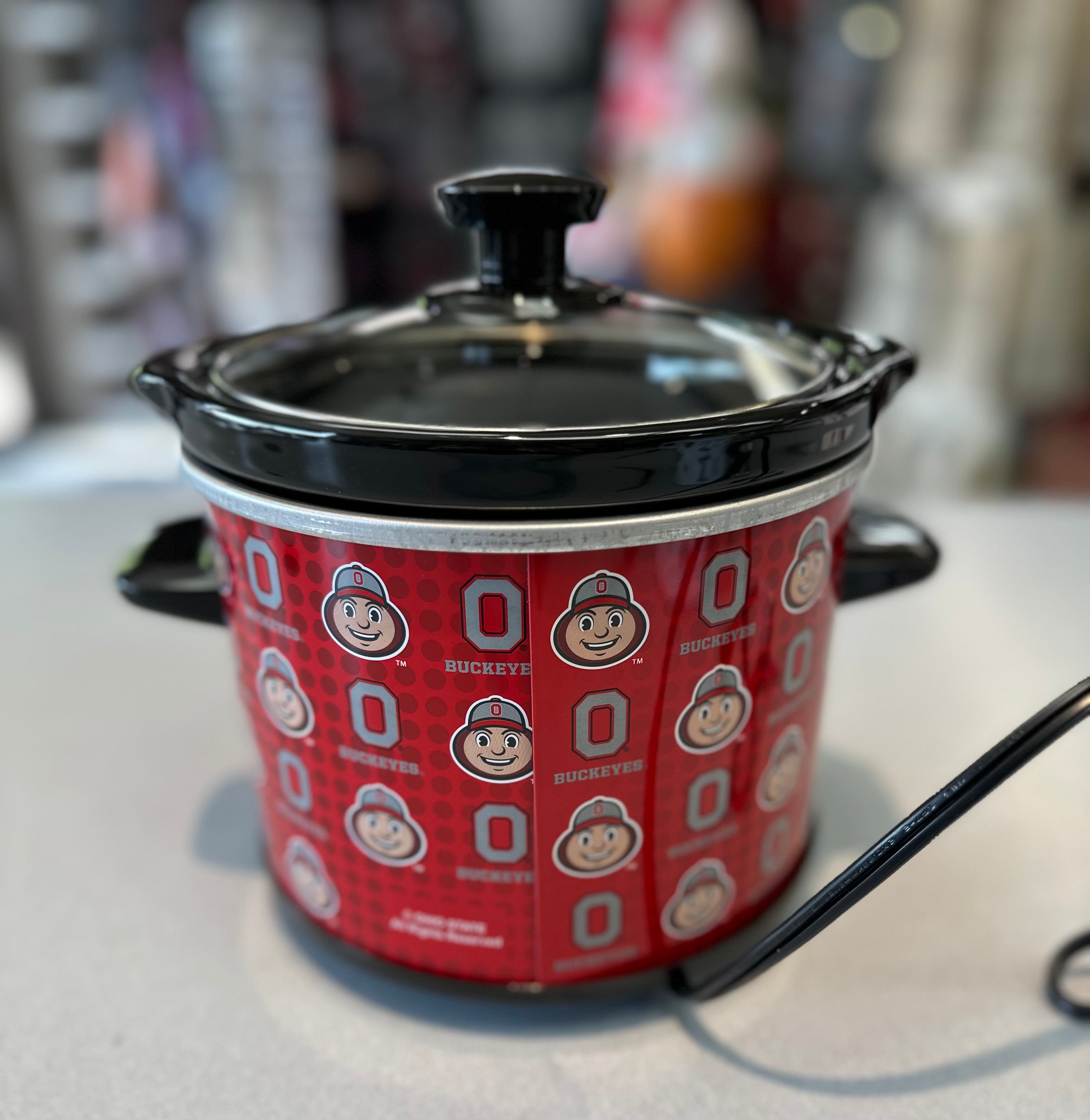 Small red container with black lid featuring a logo on a white surface
