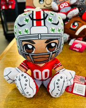 Plush toy of a football player in a helmet with green patterns on a wooden surface.
