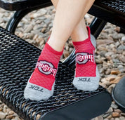 Red Ohio State socks with gray toes and heels worn by a person sitting on a black metal bench.
