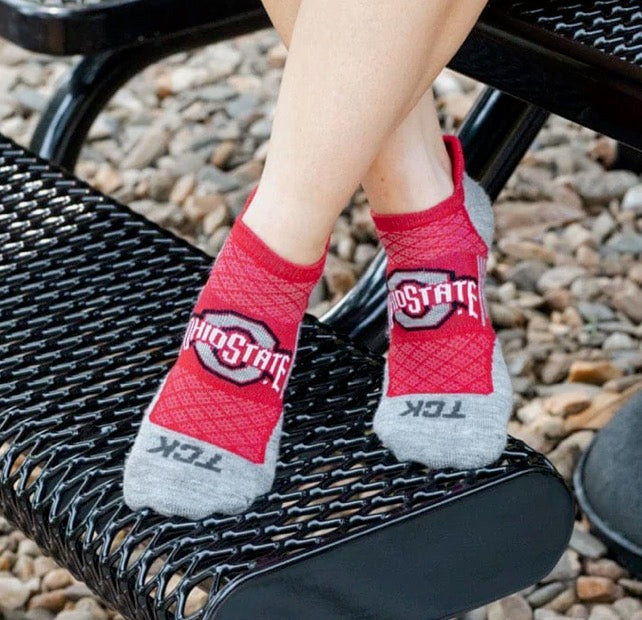 Red Ohio State socks with gray toes and heels worn by a person sitting on a black metal bench.