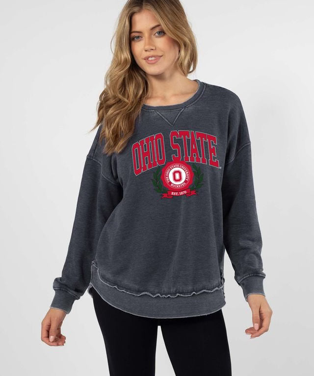 A woman modeling a dark gray washed sweatshirt with a red and white 'Ohio State' graphic on the front, paired with black pants, against a light gray studio background.