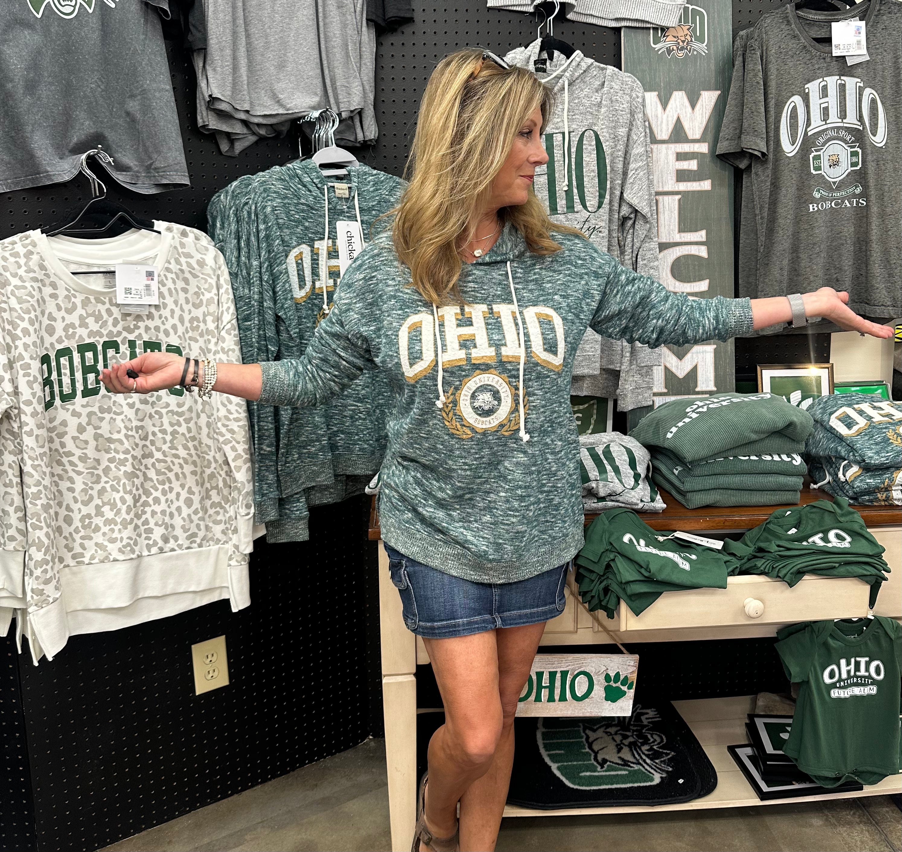 Woman wearing a green 'OHIO' sweatshirt in a store with various merchandise.