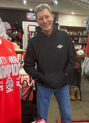 Man wearing a black hoodie with a logo in a store setting