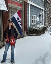 Person holding a flag with 'Open' text in front of a building with snow on the ground