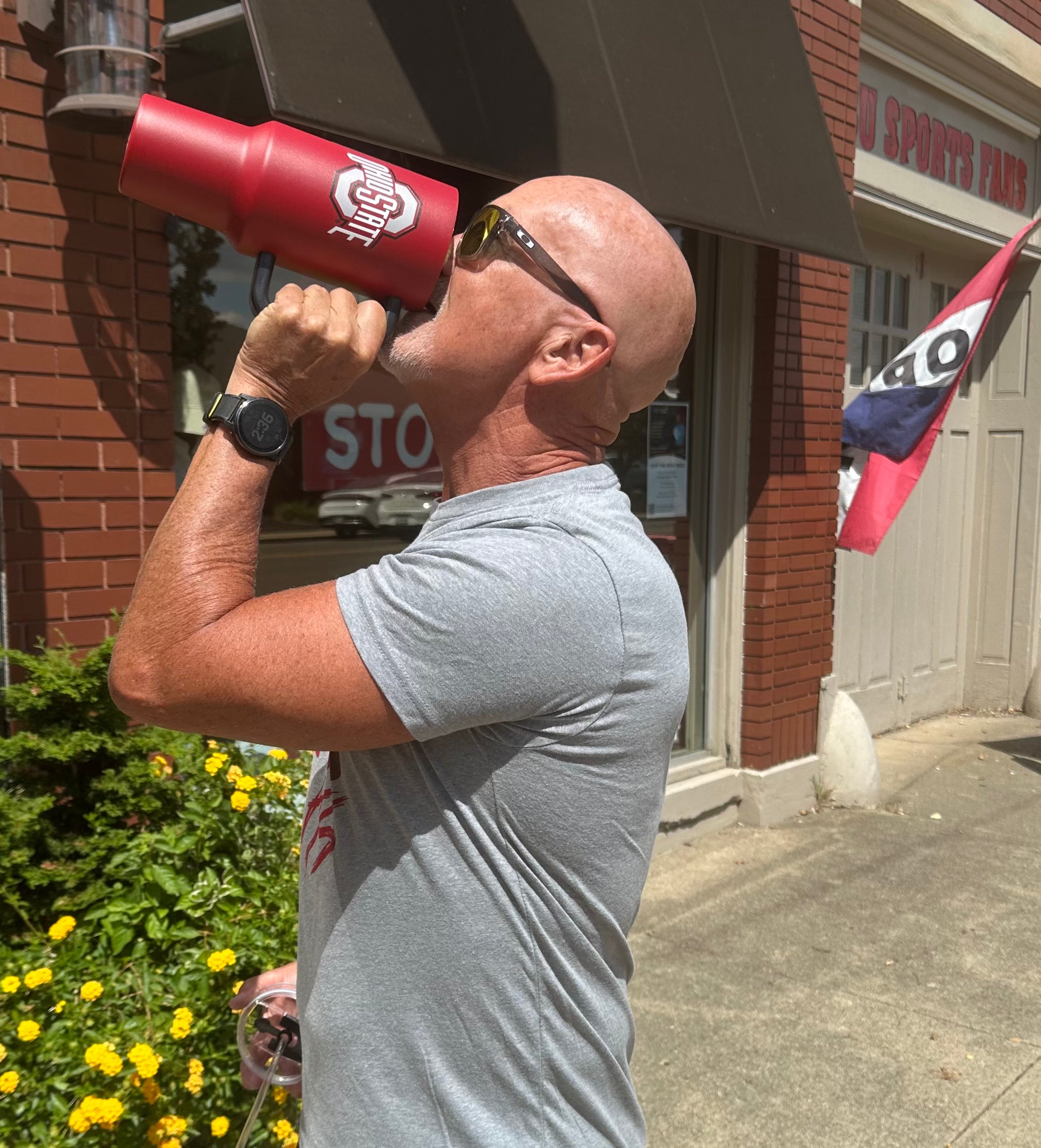 Man drinking from a red sports bottle with a megaphone in front of a store.