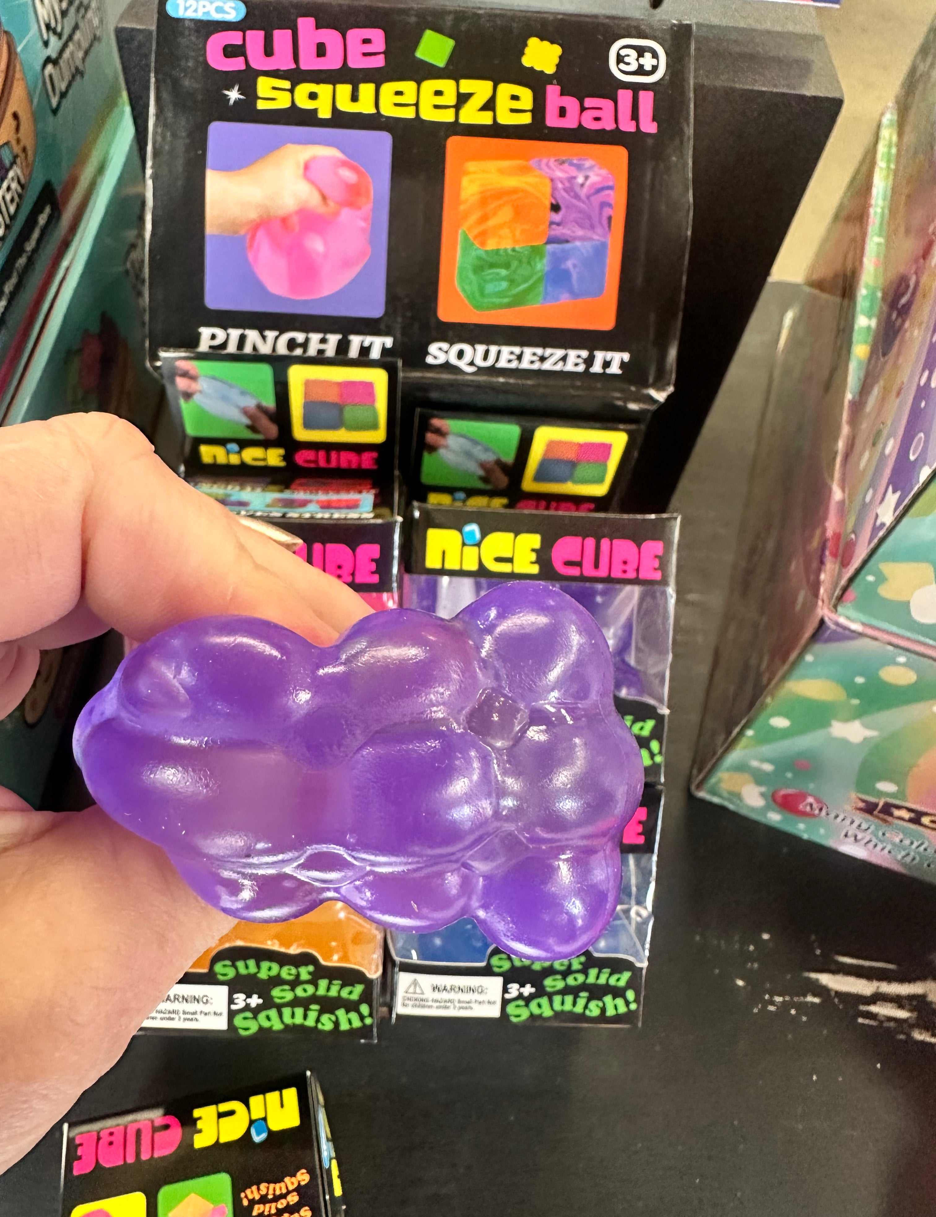 Purple cube squeeze ball held by a hand with packaging in the background