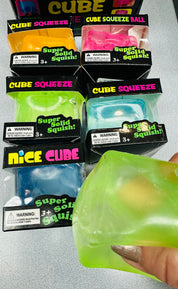 Packaged Cube Squeeze toys with a hand holding a green toy.