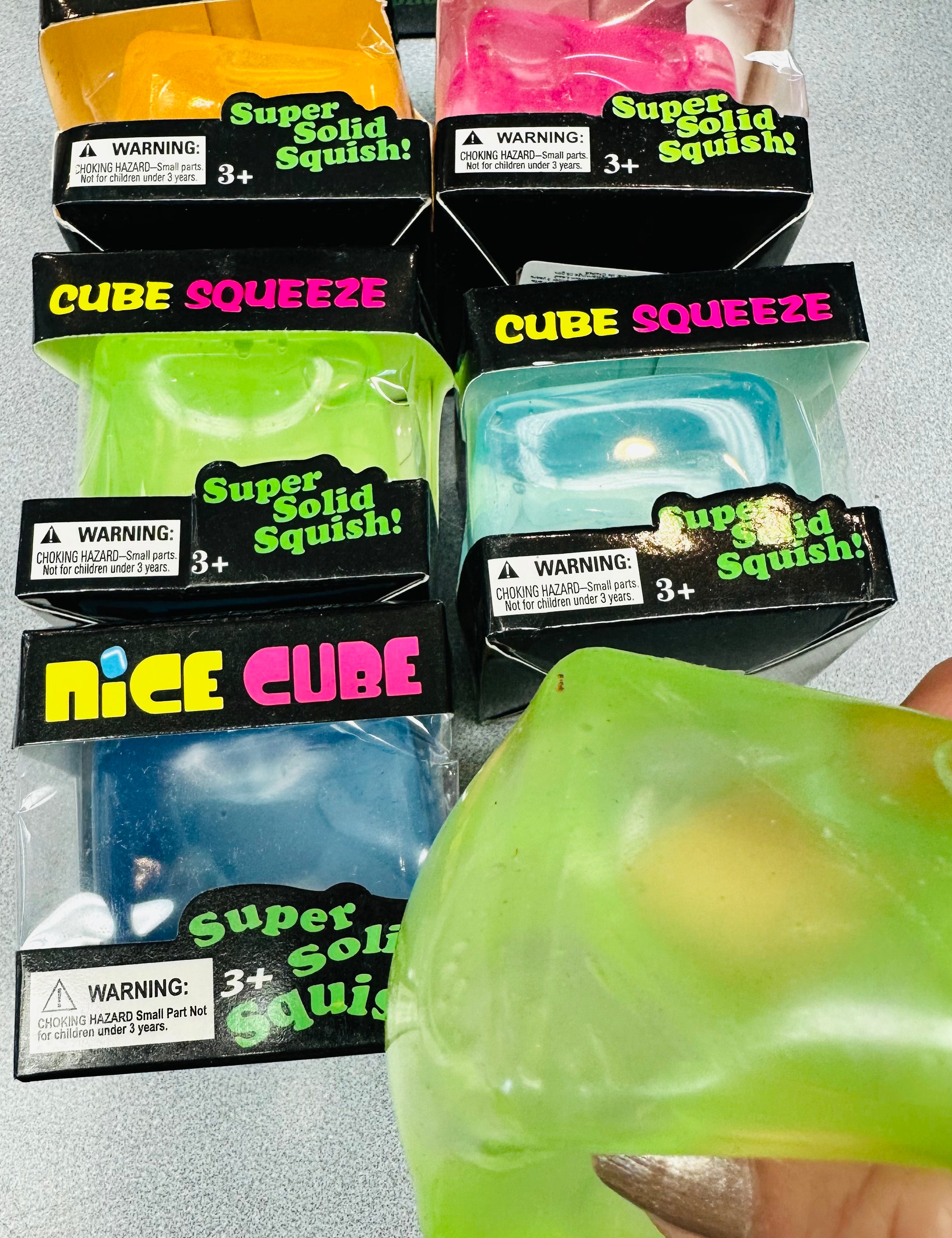 Packaged Cube Squeeze toys with a hand holding a green toy.