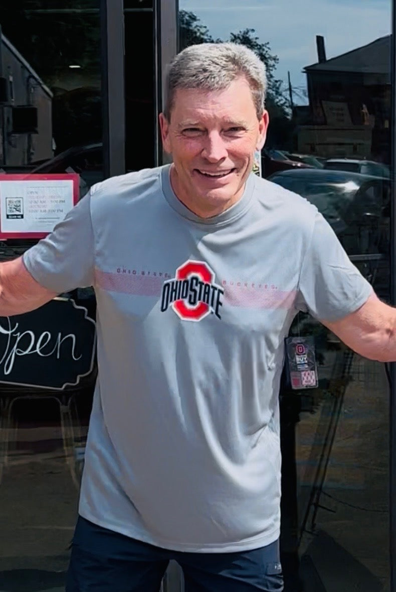 Man wearing a gray t-shirt with a logo, standing outside a building.