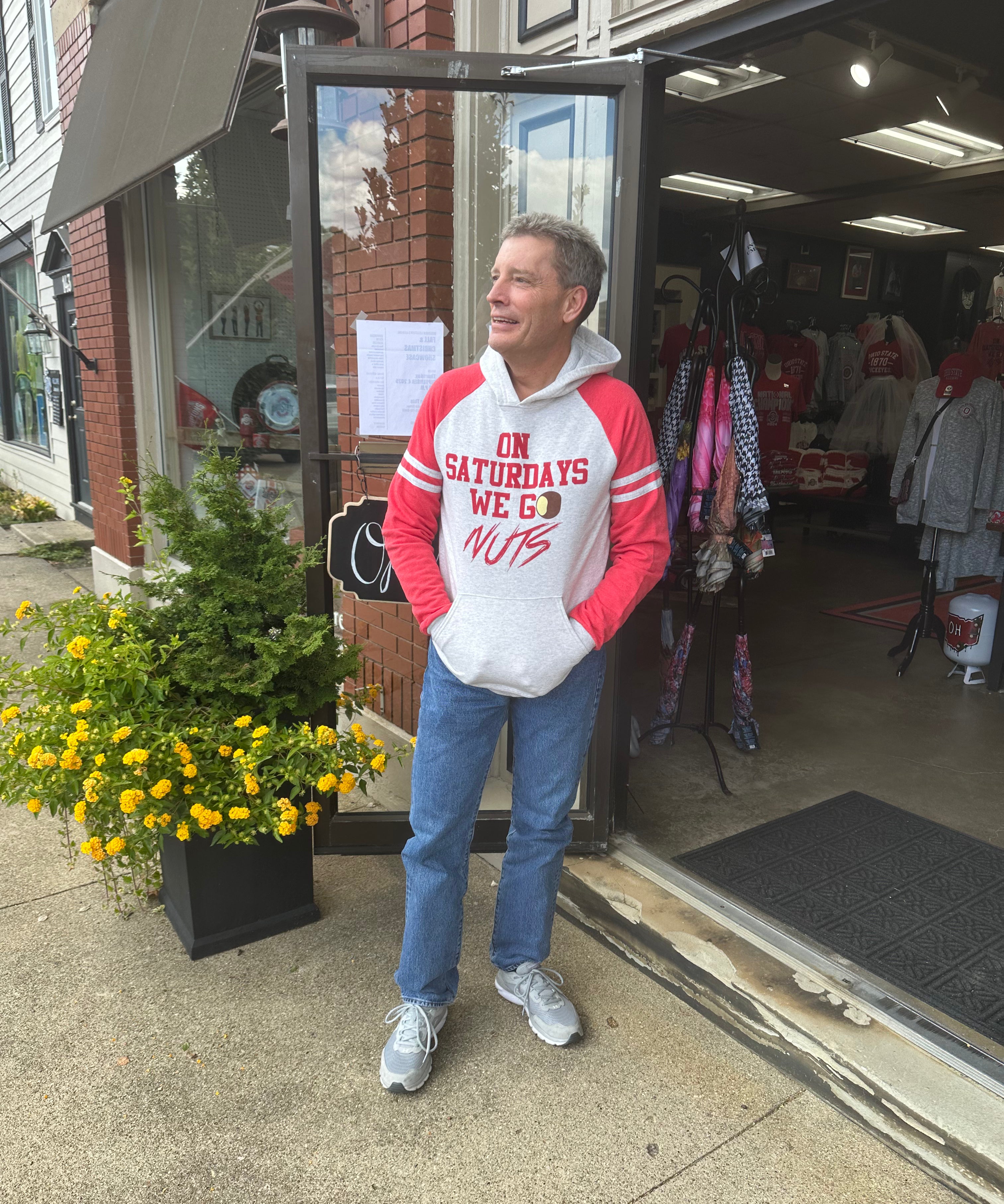 Man wearing a red and white hoodie standing outside a store with sweatshirt On Saturdays We Go Nuts.