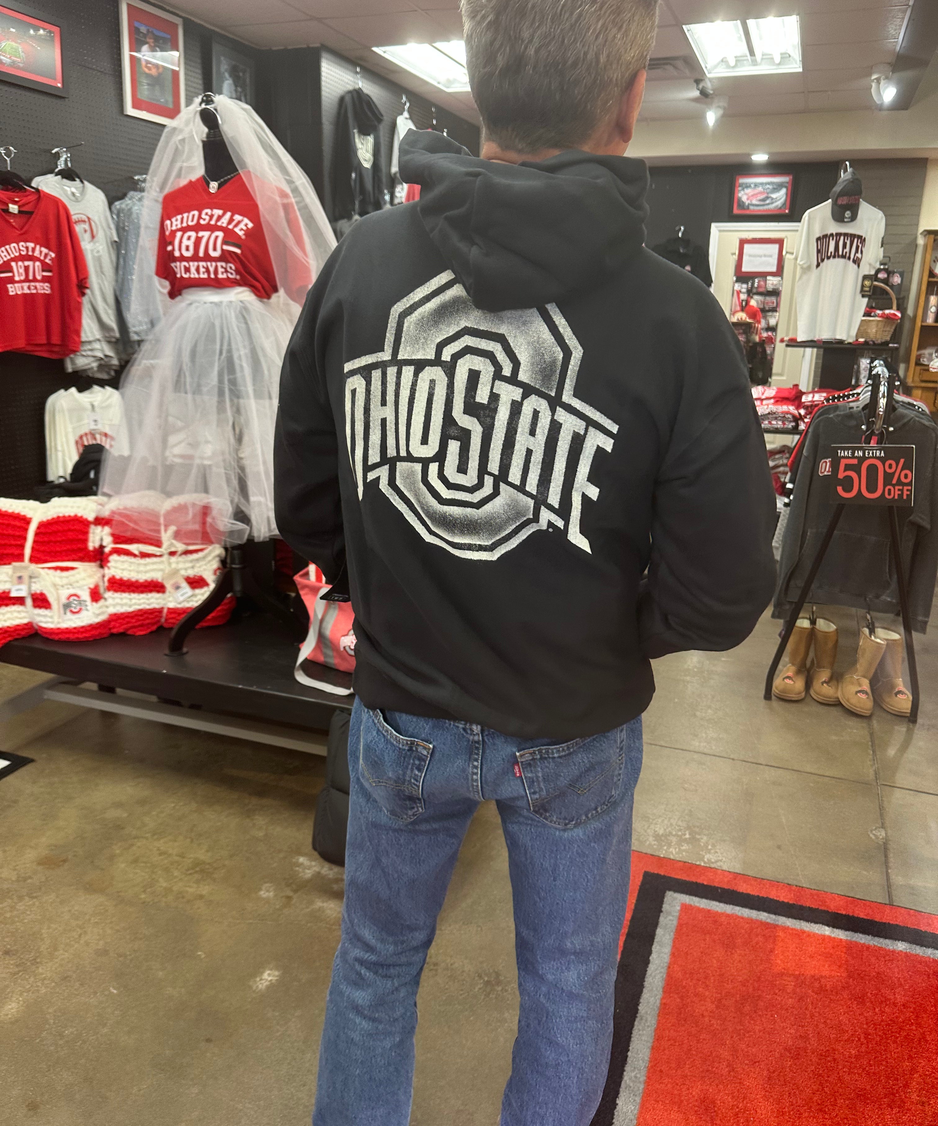 Person wearing a black hoodie with 'Ohio State' on the back in a store setting.