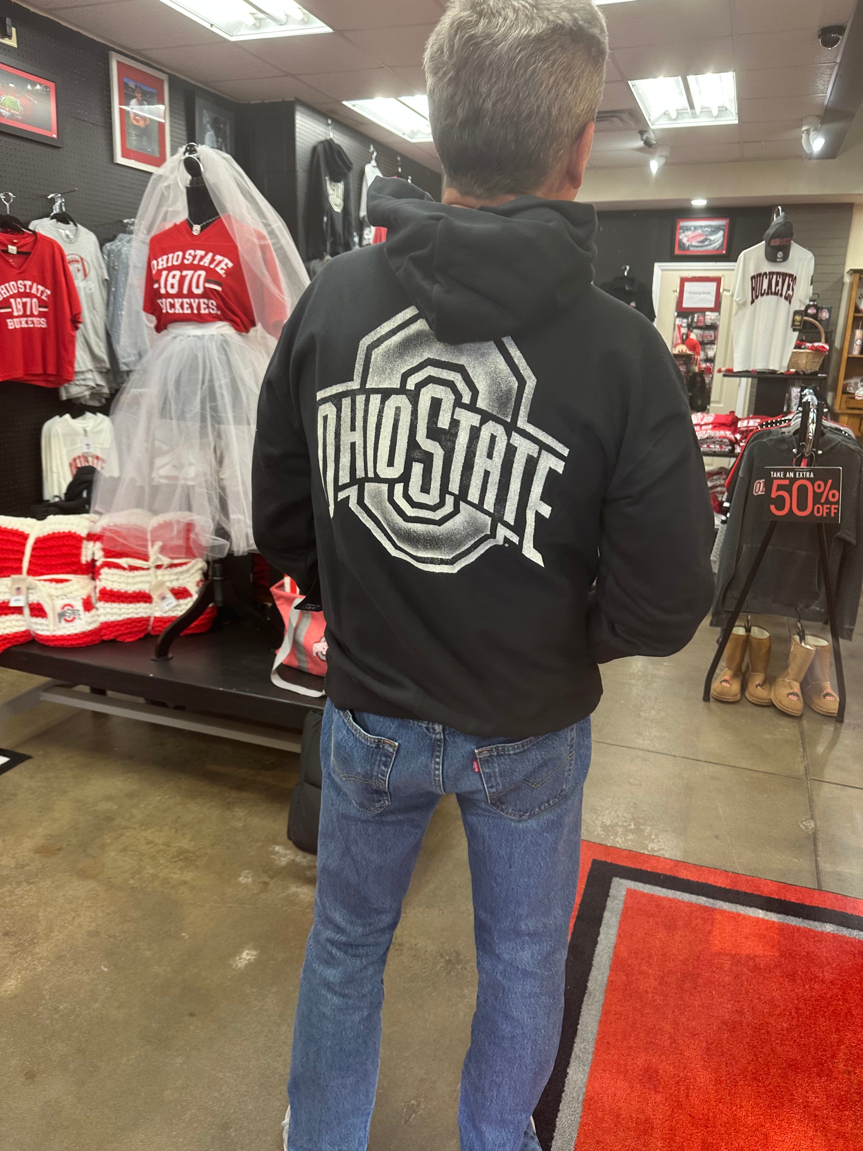 Person wearing a black hoodie with 'Ohio State' on the back in a store setting.