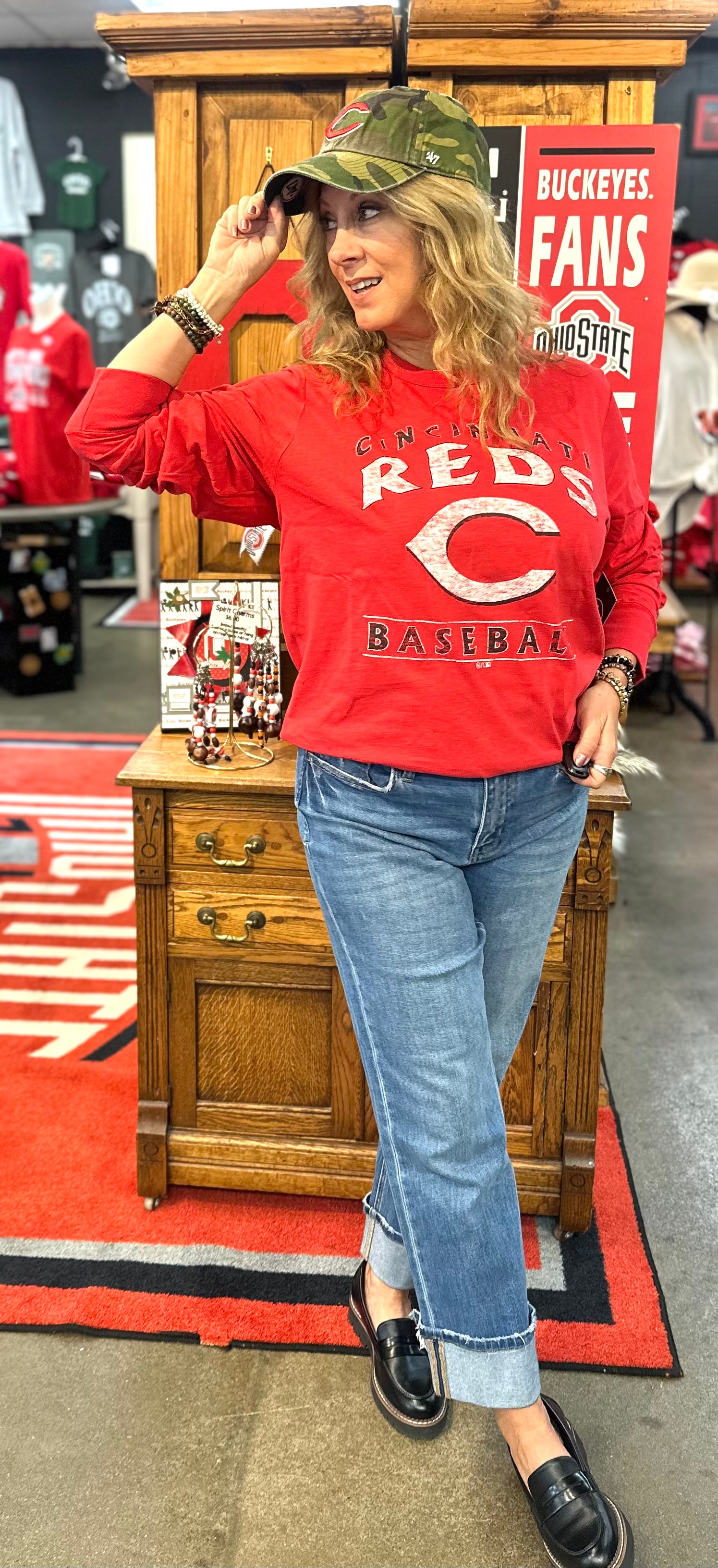 Person wearing a red 'Reds Baseball' sweatshirt and blue jeans, standing in a store with promotional signs.