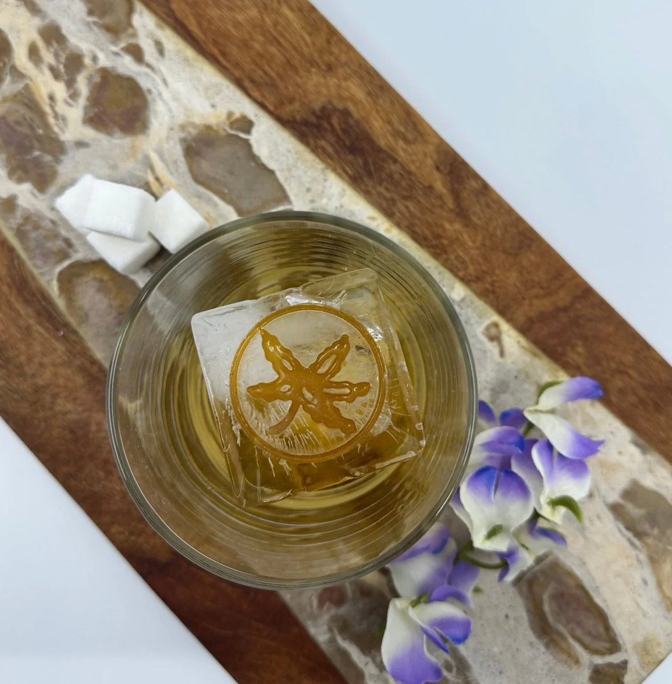 Glass of liquid with a branded ice cube on a stone surface with flowers