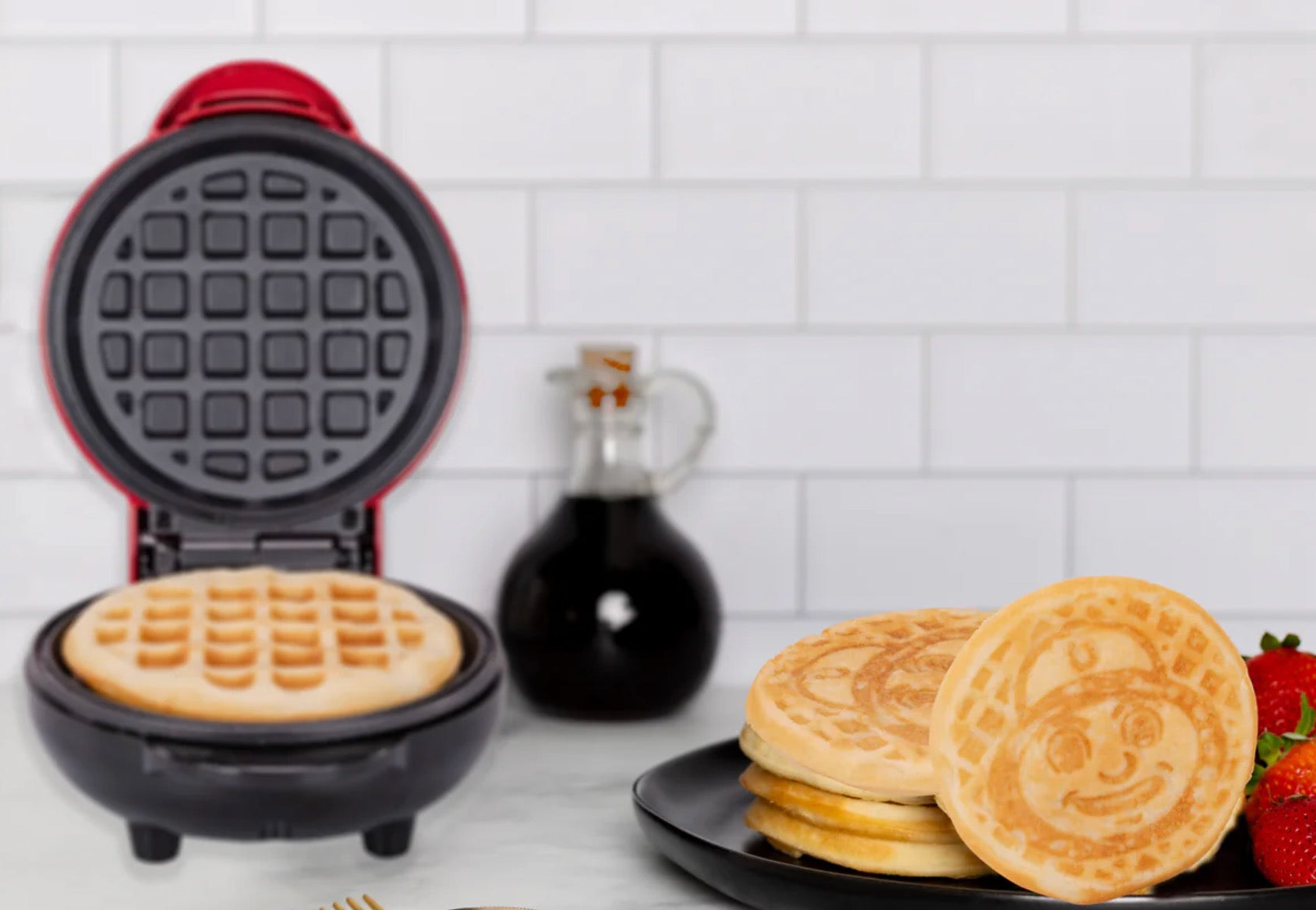 Waffle maker with waffles and a plate of pancakes on a kitchen counter.