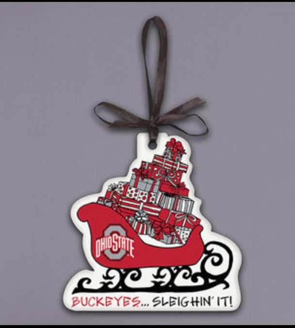 Ohio State Buckeyes Christmas ornament shaped like a sleigh filled with wrapped gifts, hanging from a dark ribbon on a solid gray background.