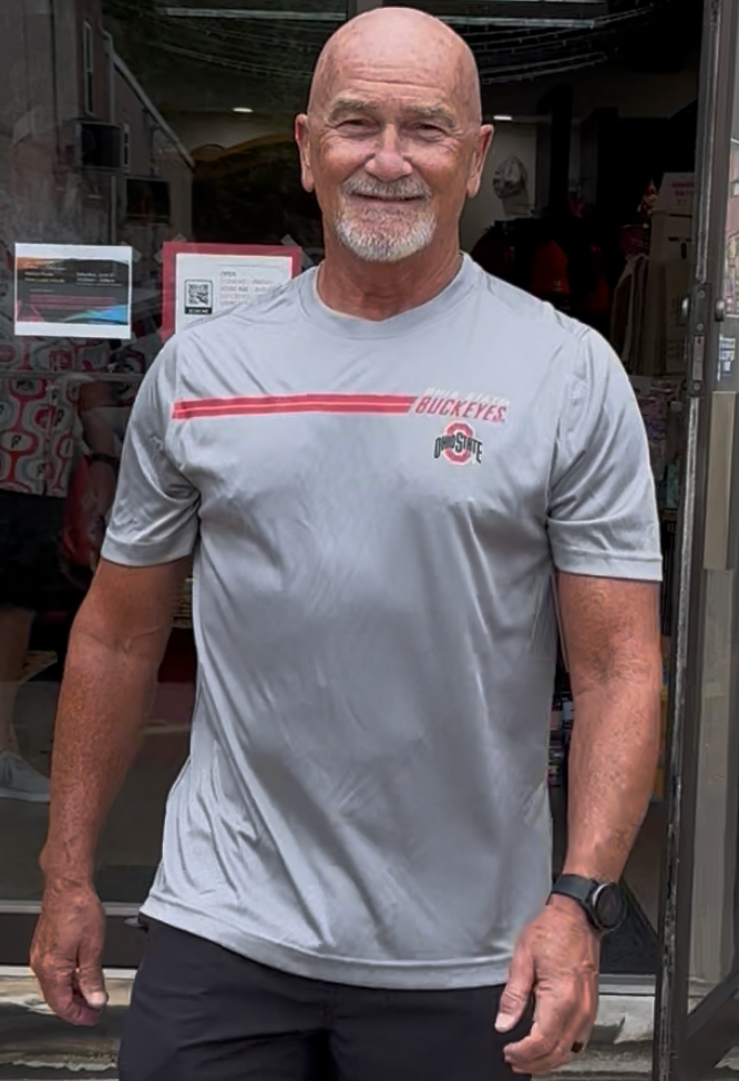 Man wearing a gray t-shirt with a logo and text, standing indoors.