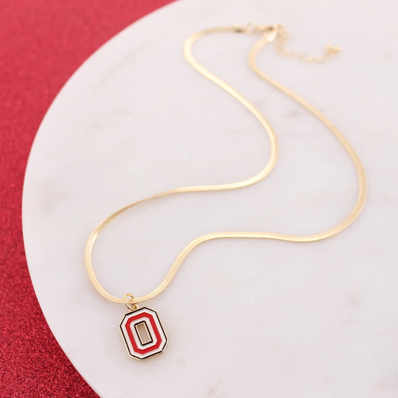Gold necklace with a red and white pendant on a white plate with a red background