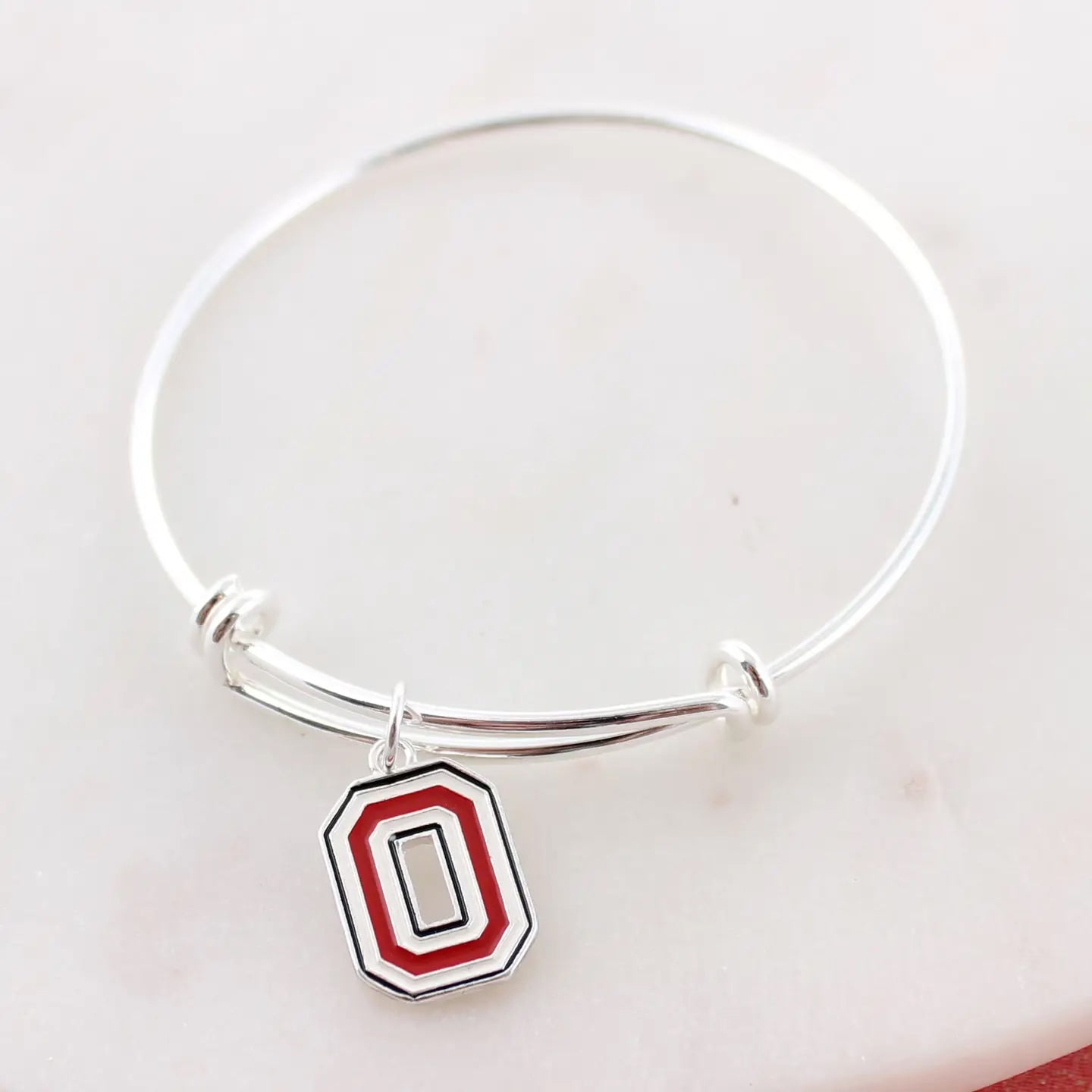 Silver bracelet with a red and black 'O' charm on a white background